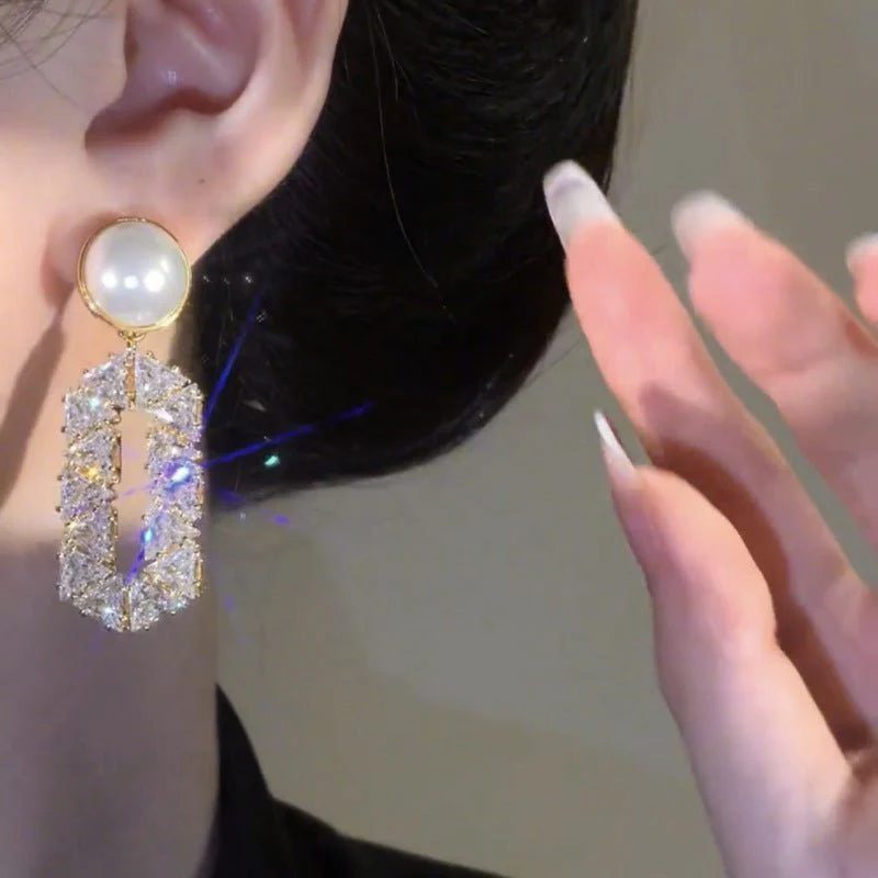 Close-up of a person wearing a decorative earring with a hand touching the ear.