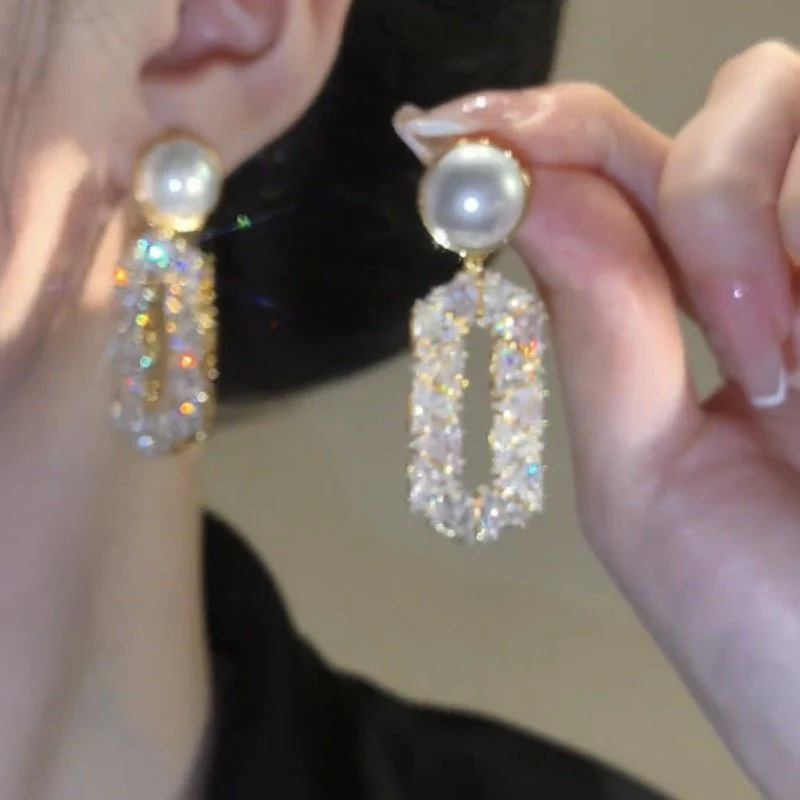 Pearl and crystal earrings held up to an ear with a neutral background