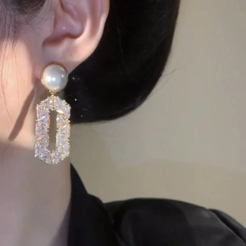 Close-up of a person wearing a pearl and crystal earring against a neutral background