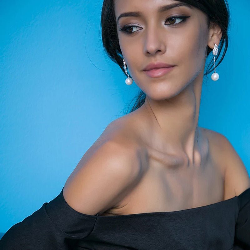 Woman wearing black off-shoulder top with pearl earrings against a blue background