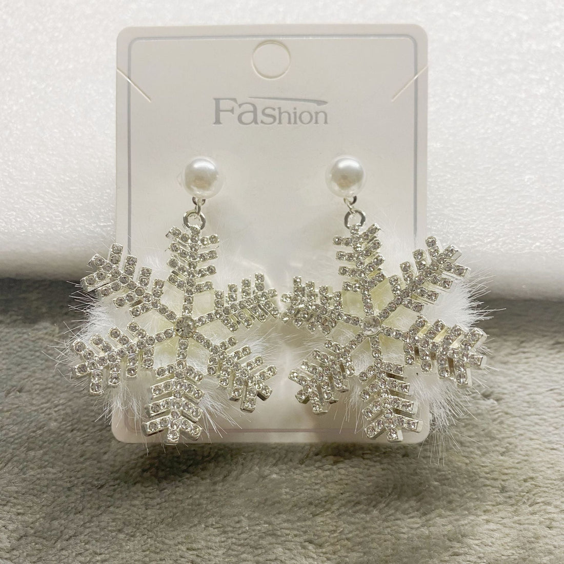 Snowflake earrings with rhinestones on a white card, placed on a textured surface.