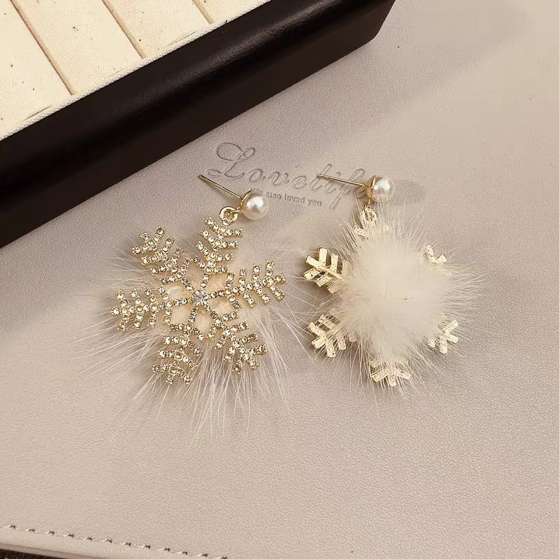 Pair of earrings with gold snowflake designs on a beige surface