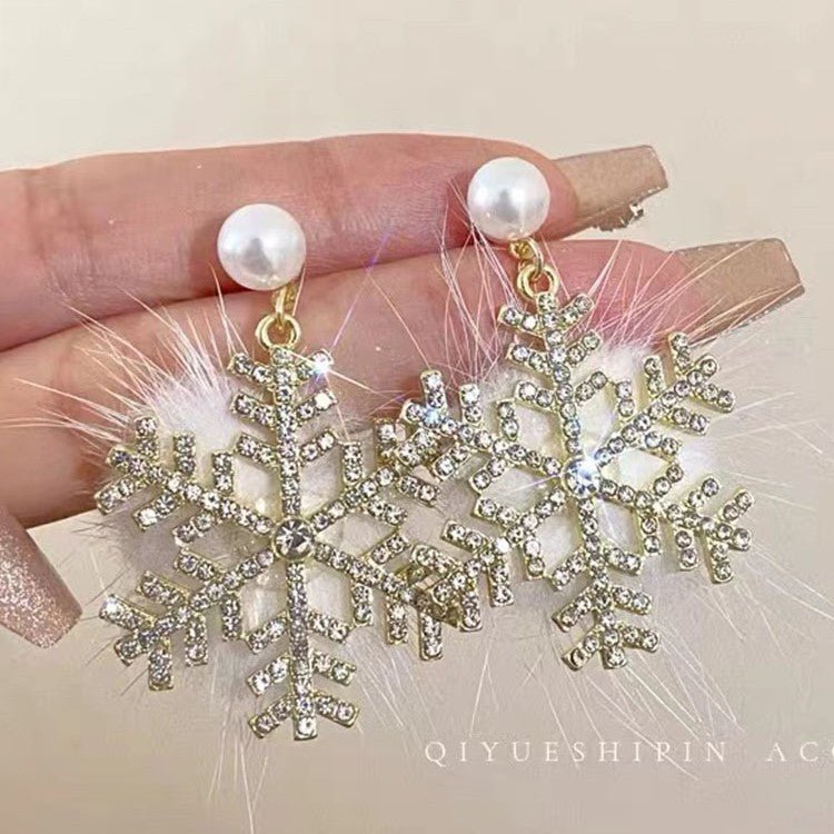 Gold snowflake earrings with pearls held by a hand against a neutral background