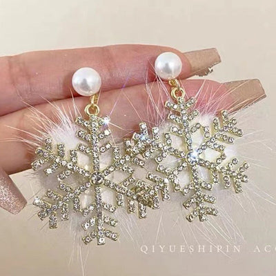Gold snowflake earrings with pearls held by a hand against a neutral background
