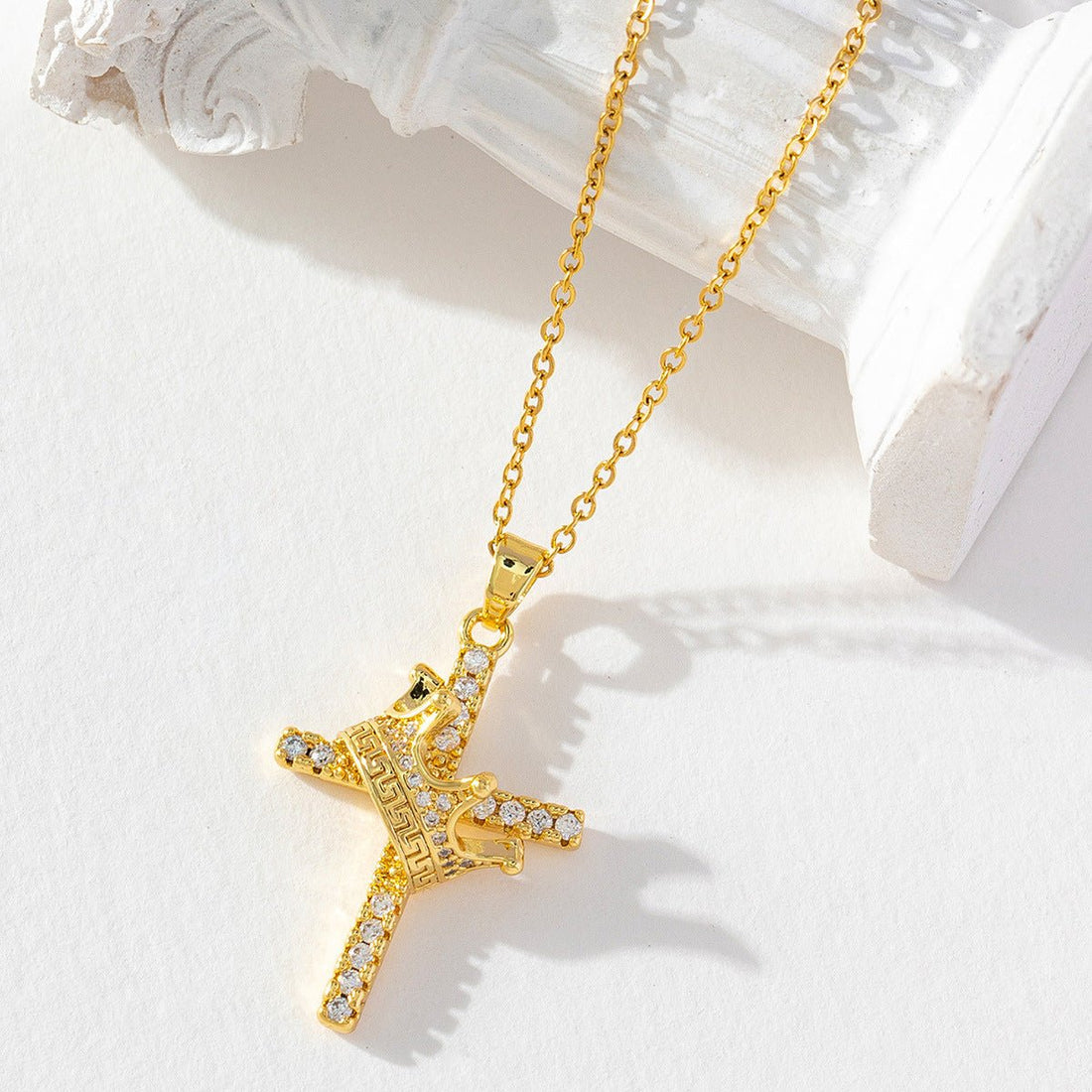 Gold cross necklace with clear stones on a white surface
