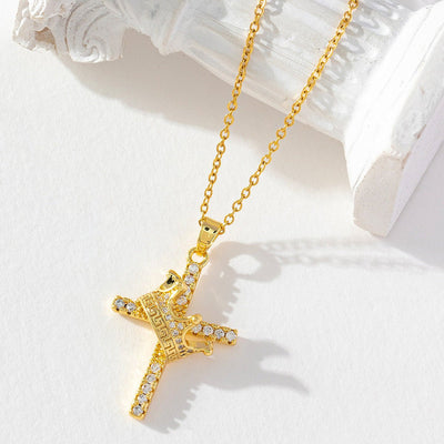 Gold cross necklace with clear stones on a white surface