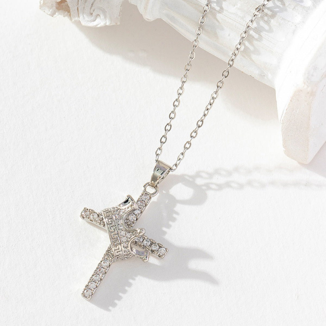 Silver cross necklace with clear stones on a white surface