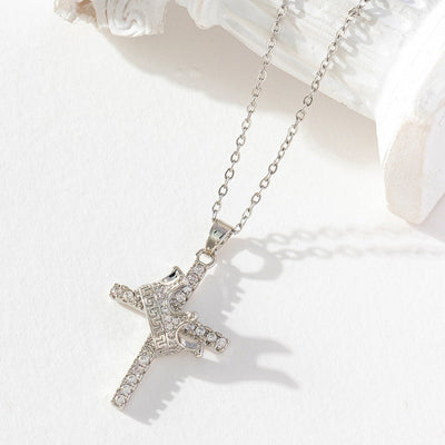 Silver cross necklace with clear stones on a white surface