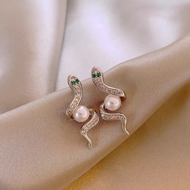 Pair of decorative earrings with pearls on a beige fabric background