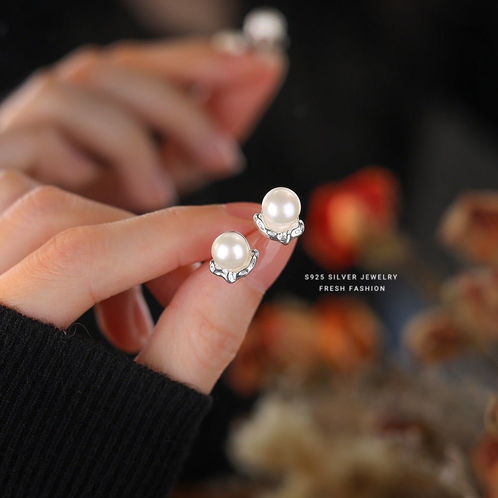 Pearl earrings held by a hand with a blurred background